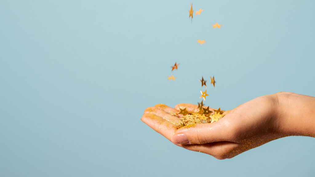 A person holding their hand out with some gold stars falling from above into their hand against a pale blue background.